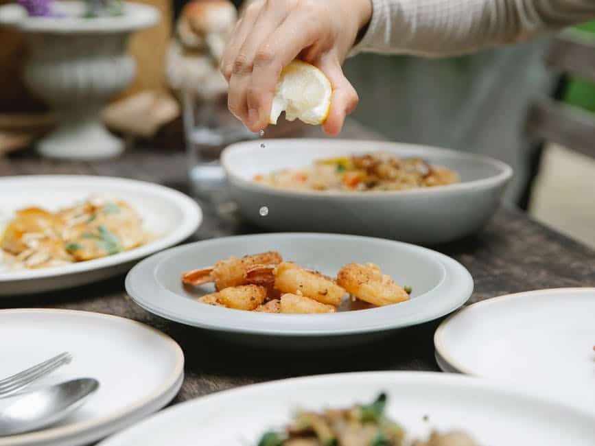woman adding lemon juice to roasted shrimps