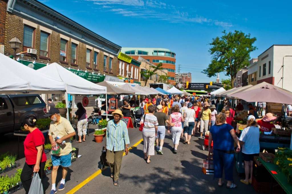 Many people shopping at a farmer's market on a sunny day