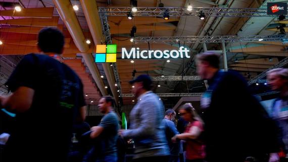 People walking under a the logo of tech giant, Microsoft.