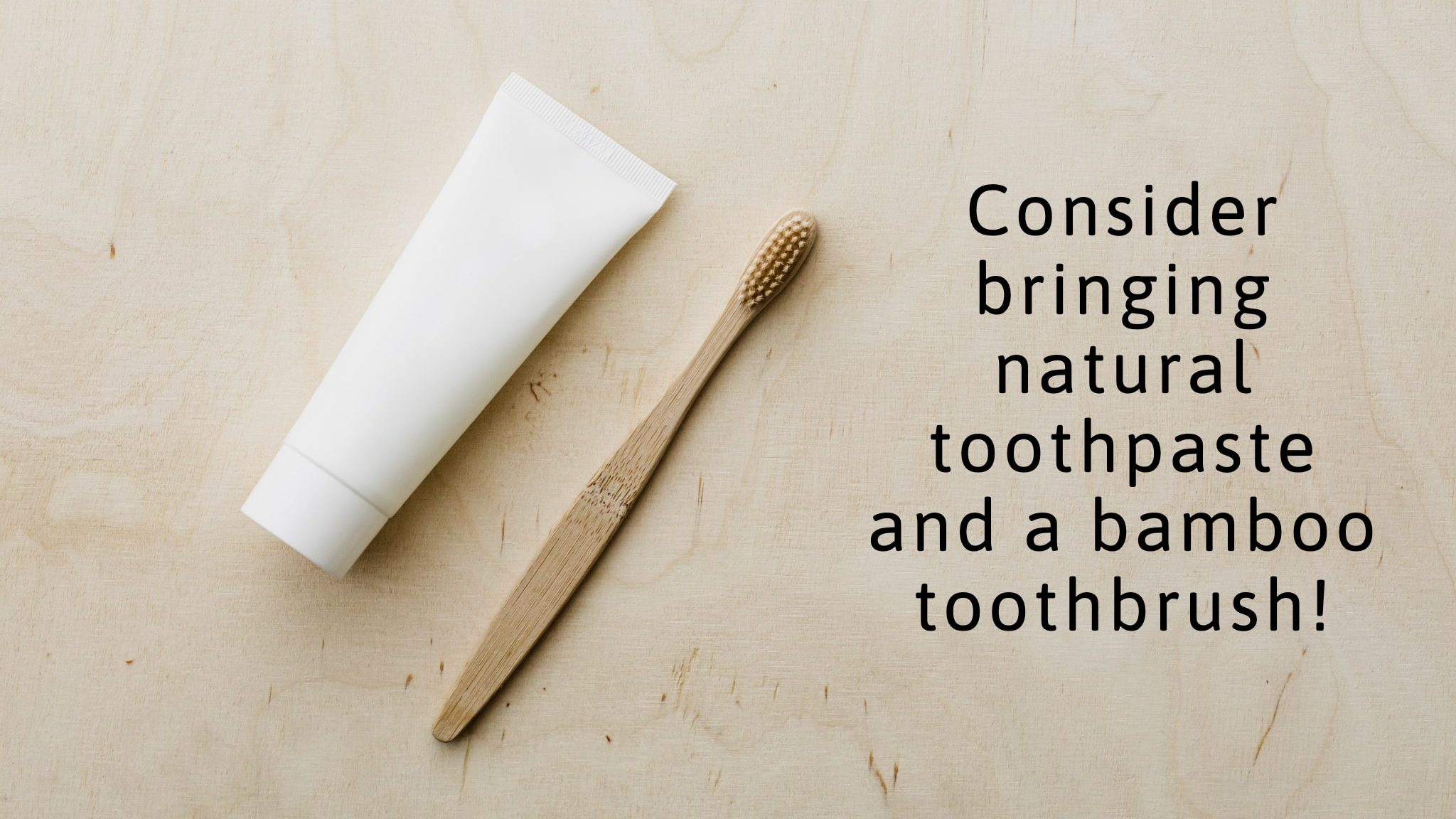 White tube of natural toothpaste pictured beside a bamboo toothbrush on a clean wooden surface. Image text reads "consider bringing natural toothpaste and a bamboo toothbrush!"