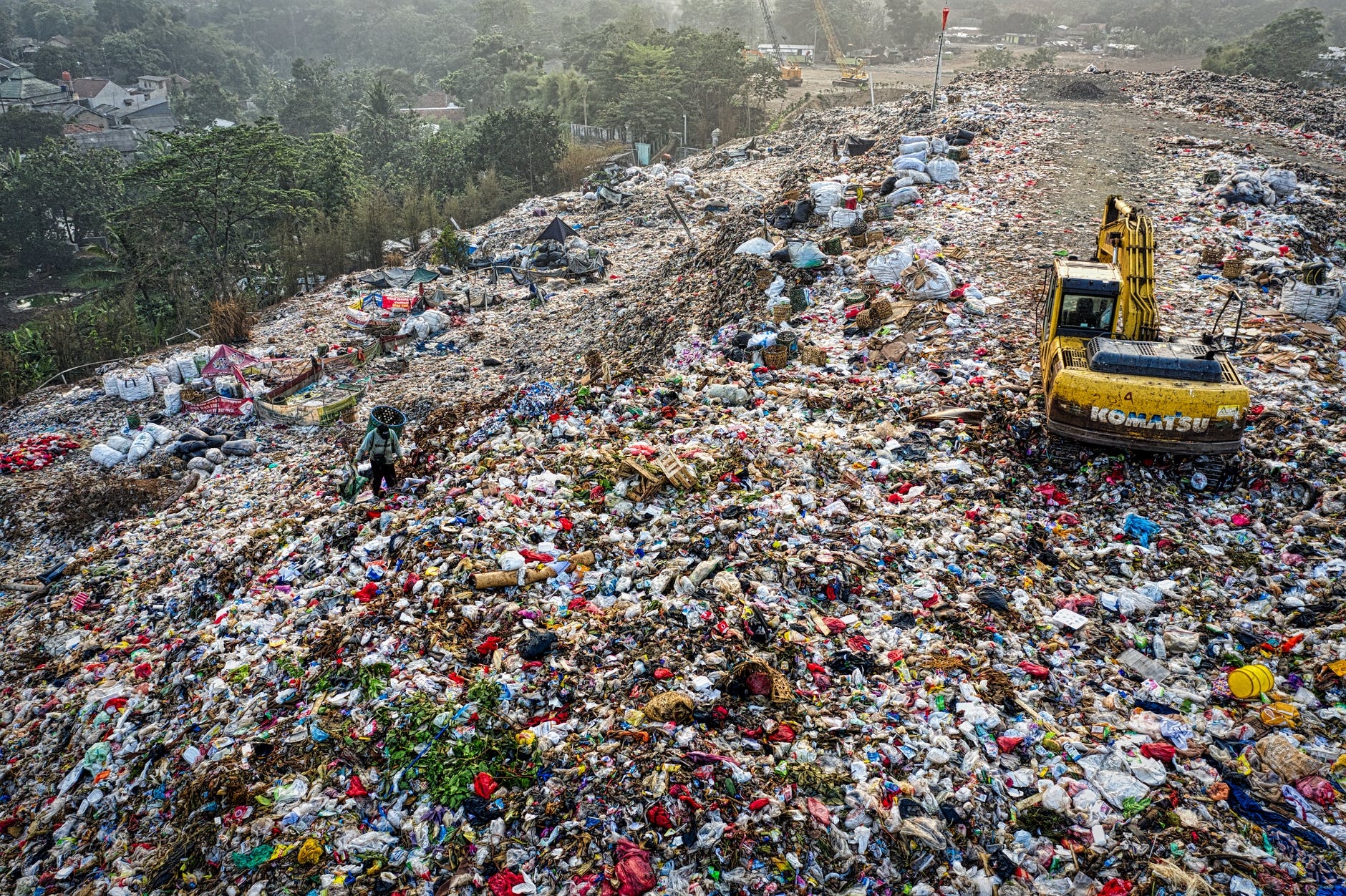 The sheer amount of waste begs for a better system. Image of an excavator  plowing through trash.